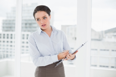 Elegant young businesswoman with graphs standing in bright officeの写真素材