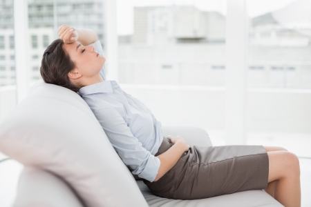 Side view of a tired beautiful well dressed young woman sitting on sofa at bright homeの写真素材