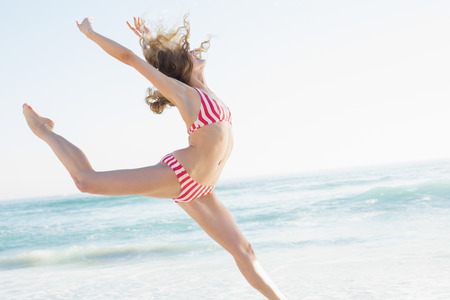 Beautiful young woman jumping on the beach wearing a red bikiniの写真素材