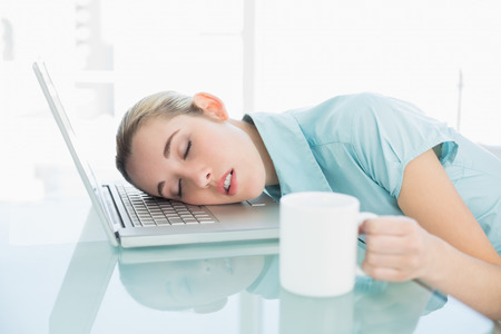 Young exhausted businesswoman sleeping sitting on her swivel chair lying with her head on her notebookの写真素材