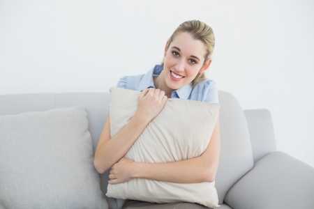 Content peaceful businesswoman sitting on couch holding a pillow smiling at cameraの写真素材