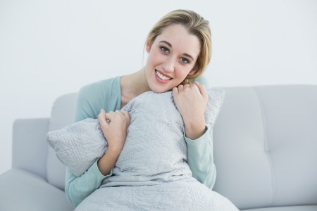 Peaceful blonde woman holding a pillow sitting on couch smiling at cameraの写真素材