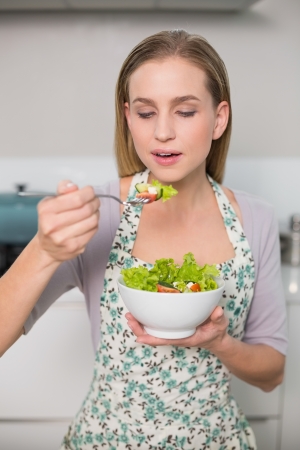 Happy gorgeous model eating salad standing in kitchenの写真素材