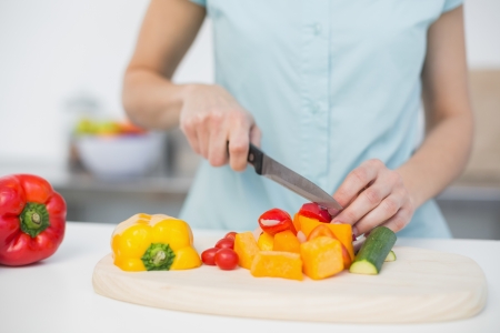 Mid section of young slender woman cutting vegetables standing in kitchenの写真素材