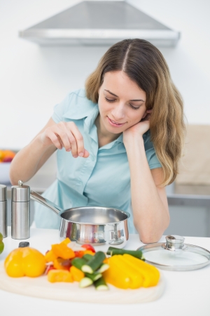 Content brunette woman cooking with vegetables standing in kitchen at homeの写真素材