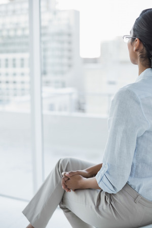 Chic dark haired businesswoman sitting in her office looking out of the windowの写真素材