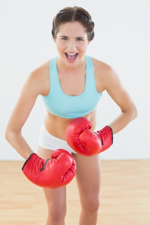Portrait of a fit woman in red boxing gloves flexing muscles at fitness studioの写真素材