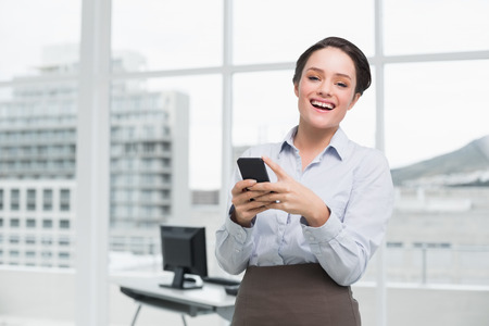 Portrait of a cheerful businesswoman holding mobile phone in a bright officeの写真素材