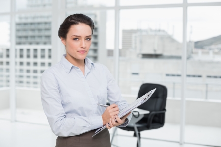 Portrait of an elegant young businesswoman with clipboard in a bright officeの写真素材