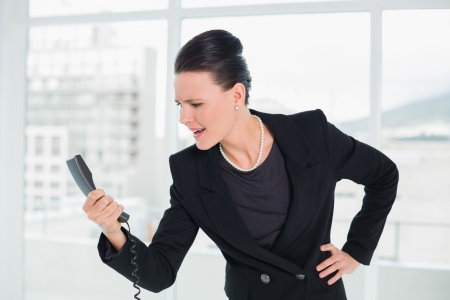 Elegant young businesswoman shouting into the phone at a bright officeの写真素材