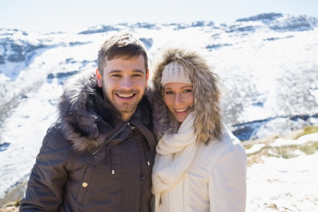 Portrait of a smiling young couple in fur hood jackets against snowed mountain rangeの写真素材
