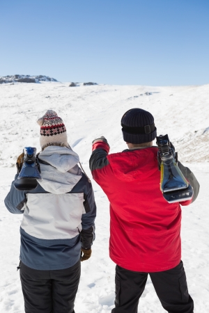 Rear view of a couple with ski boards standing on snow covered landscapeの写真素材