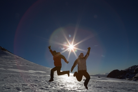 Full length of a silhouette couple jumping on snow covered landscape against the sun and clear blue skyの写真素材