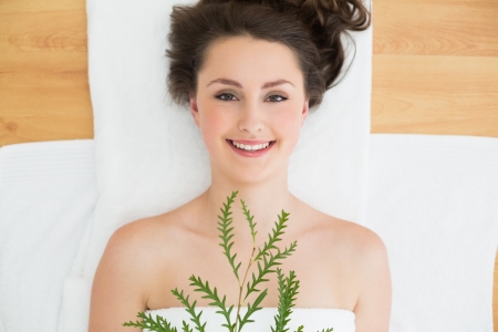 Overhead portrait of a young brunette lying with leaves on massage table in beauty salonの写真素材