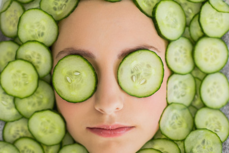 Close up of a young beautiful woman with facial mask of cucumber slices on her face at spa salonの写真素材
