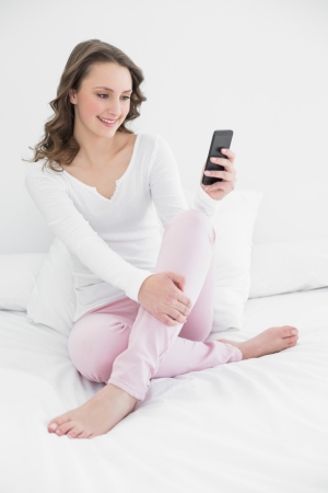 Smiling young woman looking at mobile phone in bed at homeの写真素材
