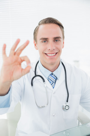 Portrait of a smiling male doctor gesturing okay sign at medical officeの写真素材