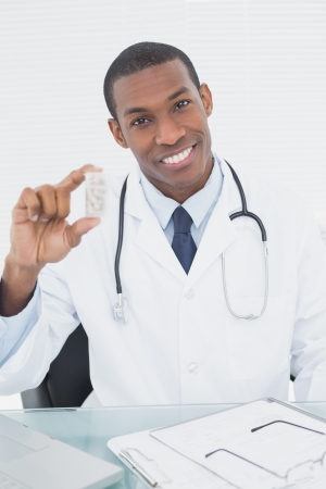 Portrait of a smiling male doctor holding a prescription bottle in medical officeの写真素材