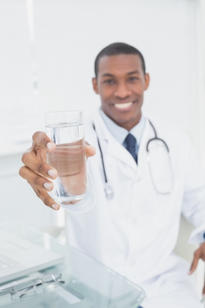 Portrait of a smiling male doctor holding out a glass of water in medical officeの写真素材
