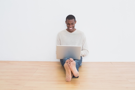 Full length of a happy casual Afro young man using laptop on floor in an empty roomの写真素材