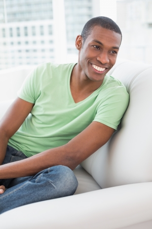 Smiling relaxed young Afro man sitting on sofa in a bright houseの写真素材