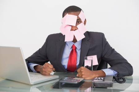 Portrait of an Afro businessman with blank notes on face and laptop over white backgroundの写真素材