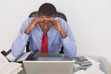 Frustrated young Afro businessman with head in hands at desk against white backgroundの写真素材