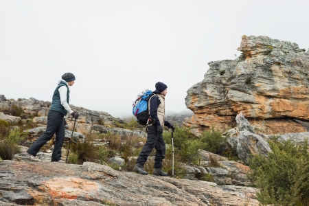 Full length side view of a couple walking through rocky landscape with trekking poles against clear...