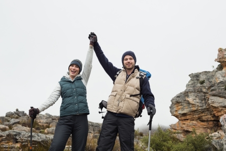 Portrait of a couple standing on rocky landscape with hands raised against clear skyの写真素材