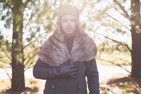 Portrait of a handsome young man in warm clothing standing in forest on a winter dayの写真素材
