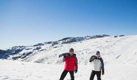 Full length of a couple carrying ski boards while walking on snow covered landscapeの写真素材