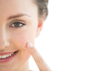 Extreme Close up of a beautiful young woman applying cream to her face over white backgroundの写真素材