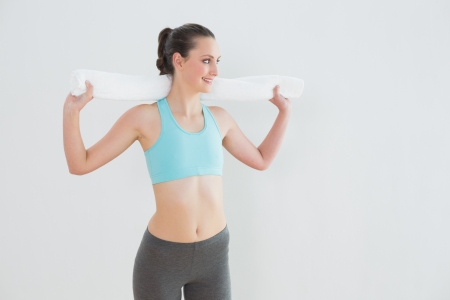 Fit young woman with towel around neck against wall at fitness studioの写真素材