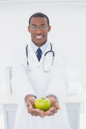 Portrait of a smiling male doctor holding a green apple at medical officeの写真素材