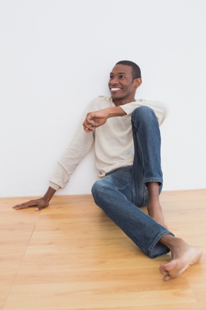 Full length of a casual Afro young man sitting on floor as he looks up to the wallの写真素材