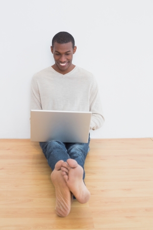 Full length of a happy casual Afro young man using laptop on floor in an empty roomの写真素材