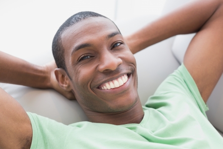 Close up portrait of a smiling relaxed young Afro man lying on sofa in a houseの写真素材