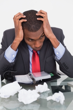 Frustrated young Afro businessman with head in hands at desk against white backgroundの写真素材