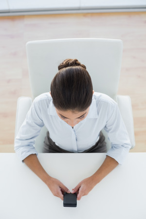 High angle view of an elegant businesswoman text messaging through mobile phone in officeの写真素材
