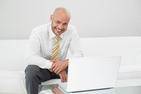 Portrait of a smiling elegant young businessman using laptop on sofa at homeの写真素材