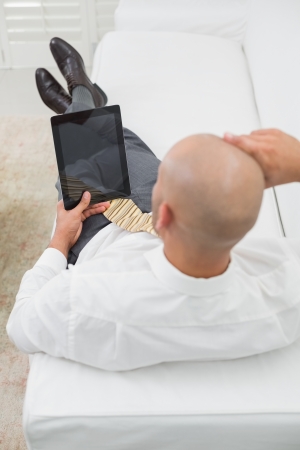 High angle view of a young bald businessman using digital tablet on sofa at homeの写真素材