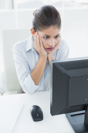Worried young businesswoman looking at computer in a bright officeの写真素材