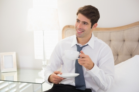 Smiling well dressed man with a cup of tea in bed at homeの写真素材