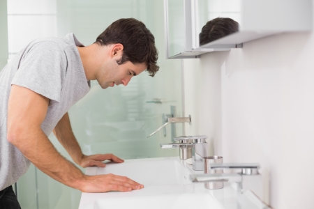 Side view of a tensed young man at washbasin in bathroomの写真素材