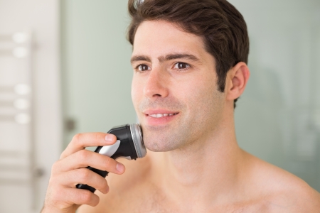 Smiling handsome young shirtless man shaving with electric razorの写真素材