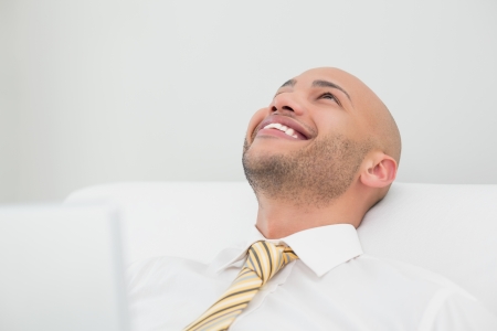 Close up of a smiling elegant young businessman looking up on sofa at homeの写真素材