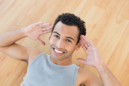 High angle portrait of a smiling young man doing abdominal crunches on parquet floorの写真素材