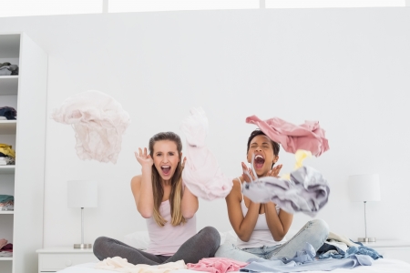 Two surprised pretty female friends with clothes up on bed at homeの写真素材