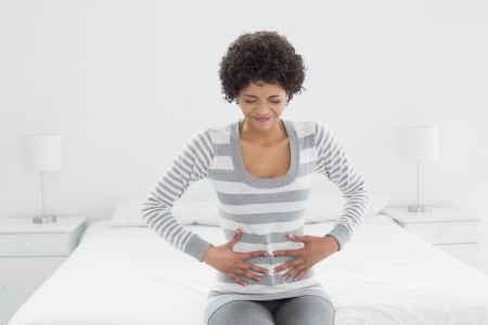 Casual young woman with stomach pain sitting in bed at homeの写真素材
