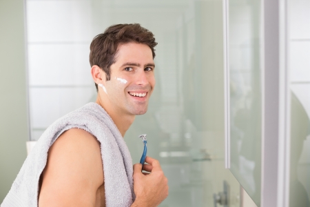 Side view portrait of a smiling handsome young man shaving in the bathroomの写真素材